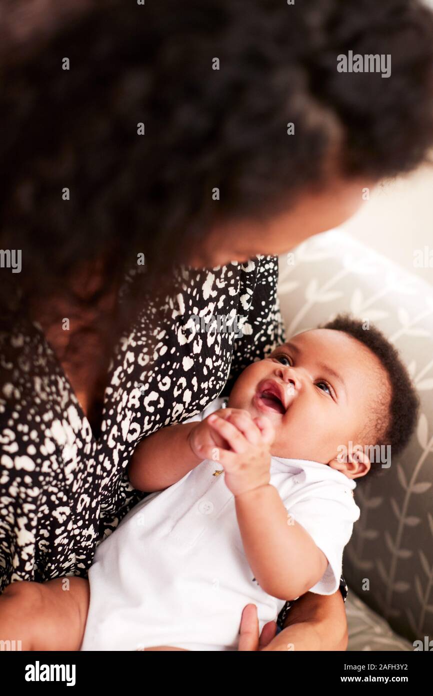 Loving Mother Sitting In Chair Cuddling Baby Son In Nursery At Home Stock Photo