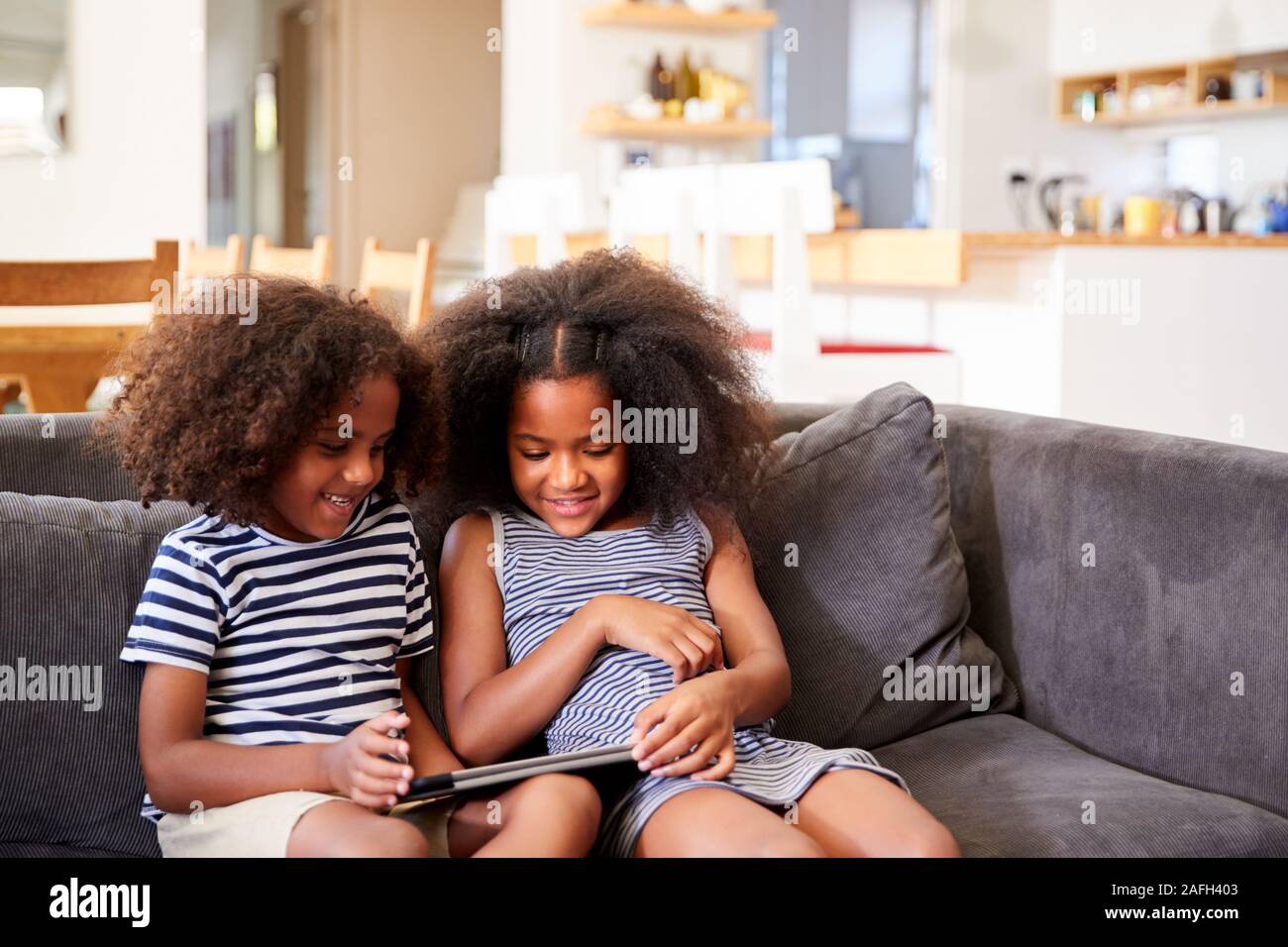 Brother And Sister Sitting On Sofa At Home Playing With Digital Tablet Stock Photo