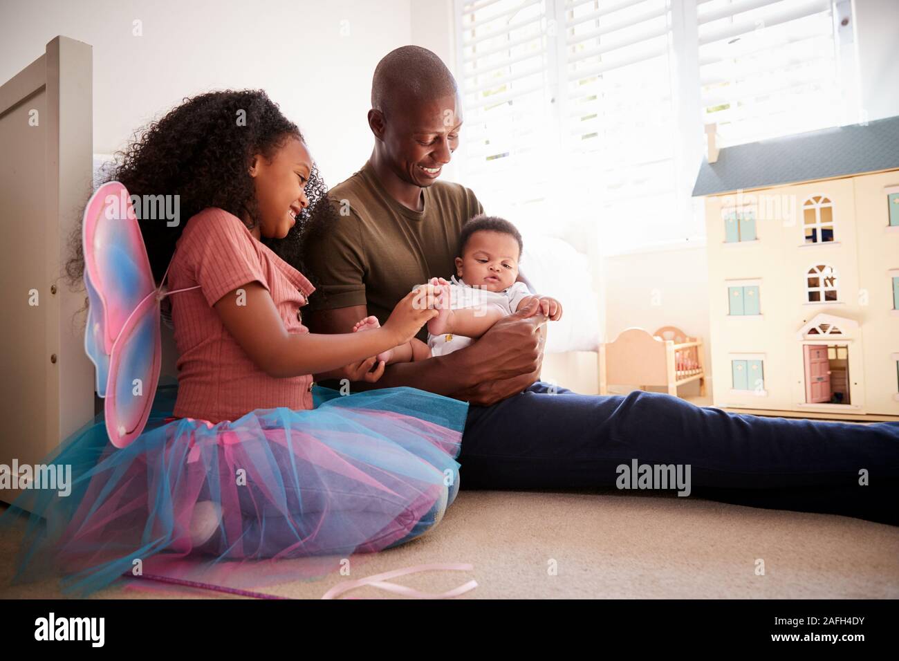 Father And Daughter Sitting In Bedroom With Baby Brother Stock Photo