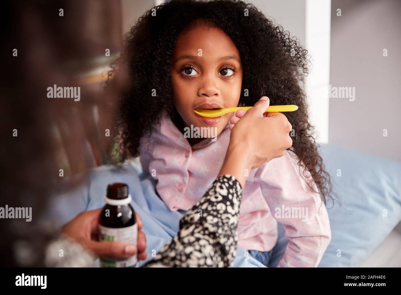 Mother Giving Sick Daughter Ill In Bed Medicine From Bottle Stock Photo