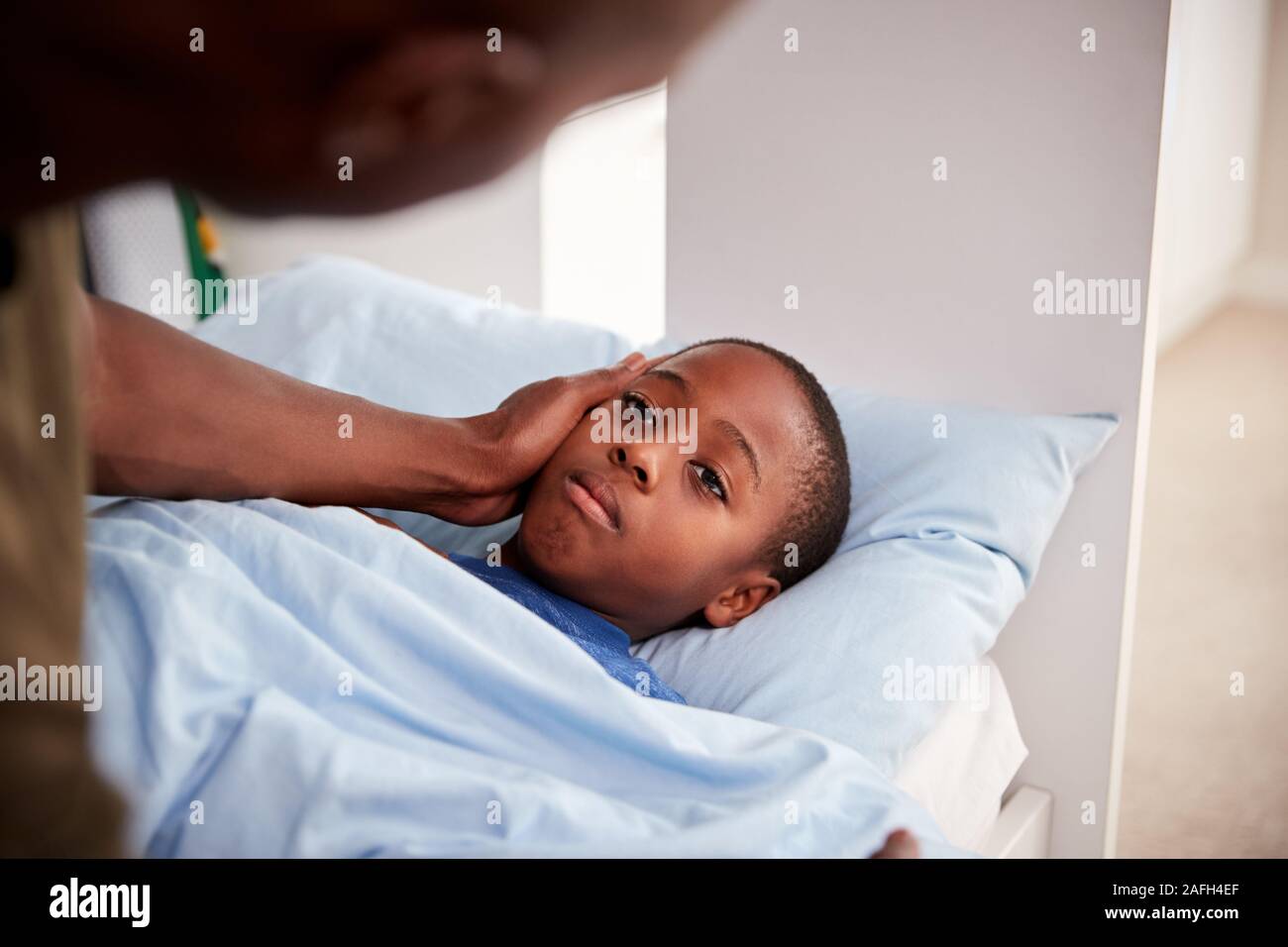 Father Caring For Sick Son Lying  Ill In Bed At Home Stock Photo