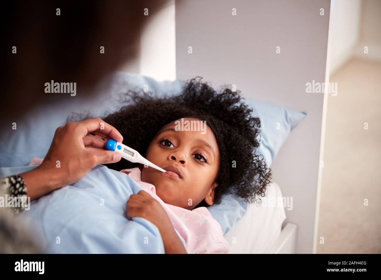 Mother Caring For Sick Daughter Ill In Bed Taking Temperature With Thermometer Stock Photo