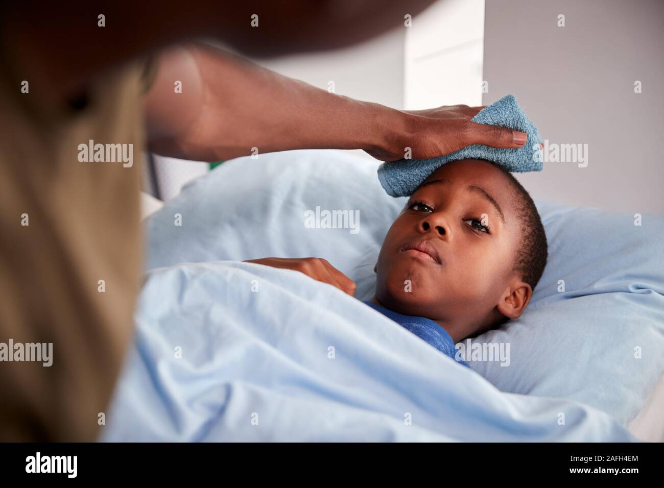 Father Caring For Sick Son Ill In Bed With Temperature Stock Photo