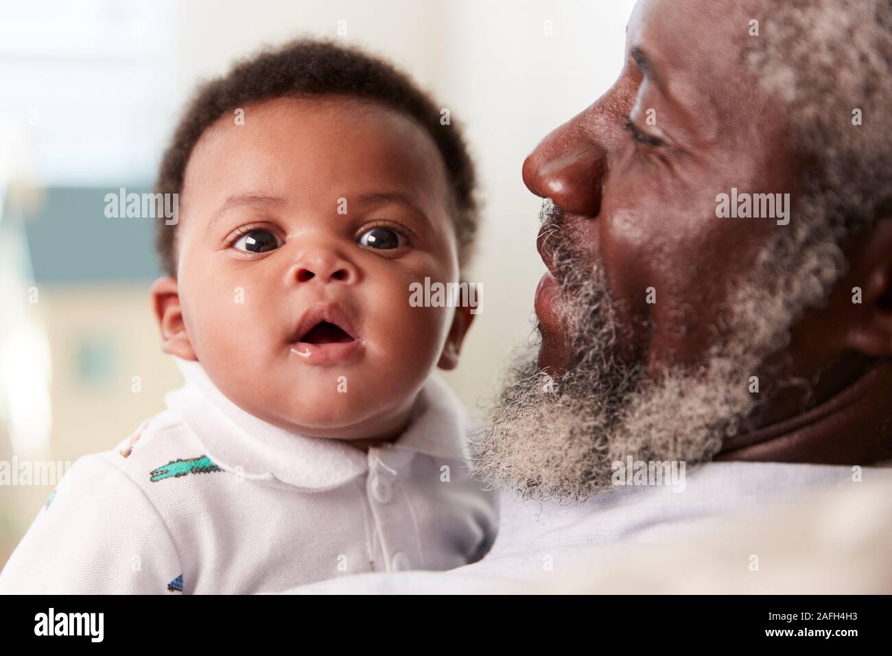 Proud Grandfather Cuddling Baby Grandson In Nursery At Home Stock Photo