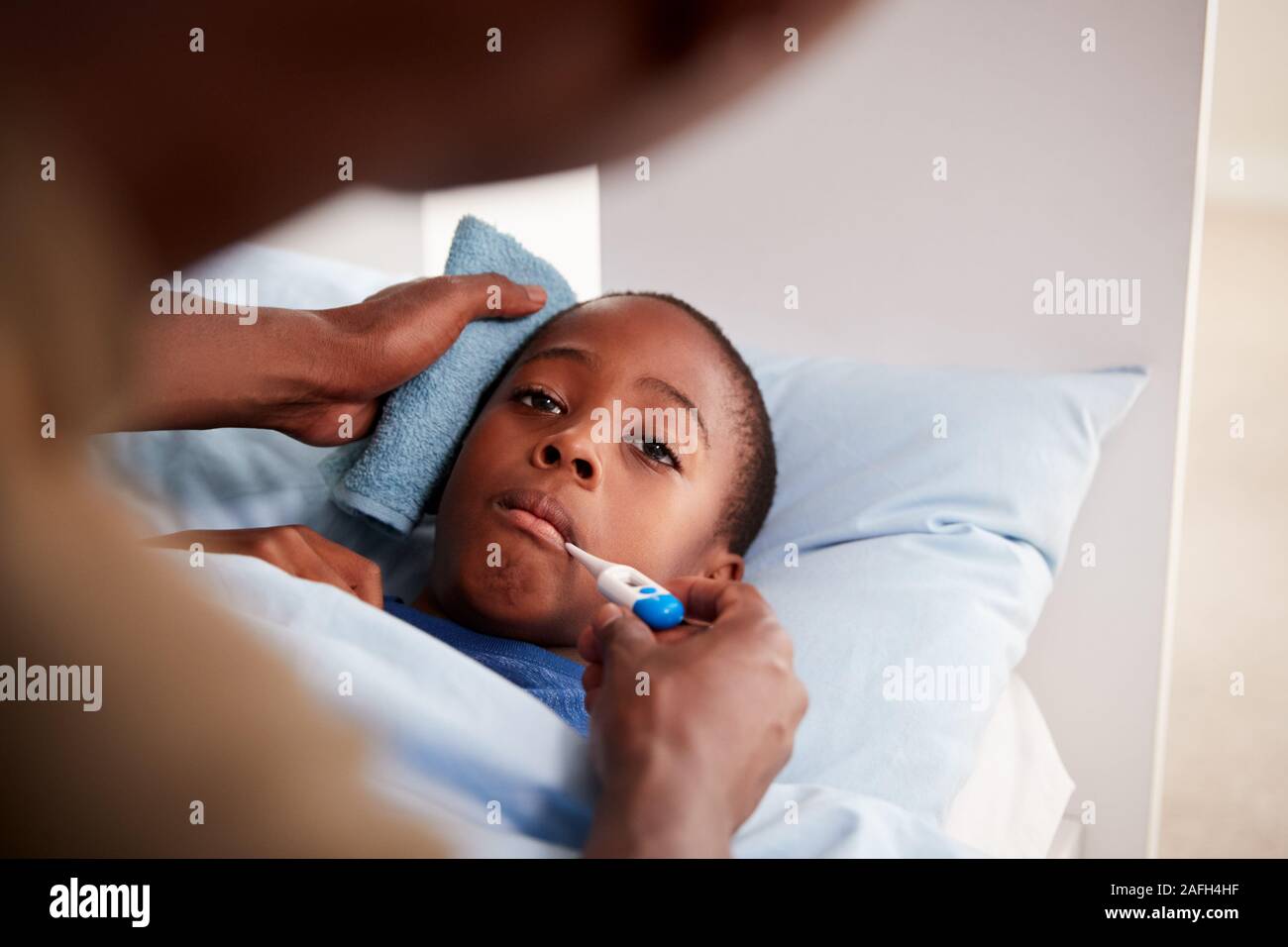 Father Caring For Sick Son Ill In Bed Taking Temperature With Thermometer Stock Photo