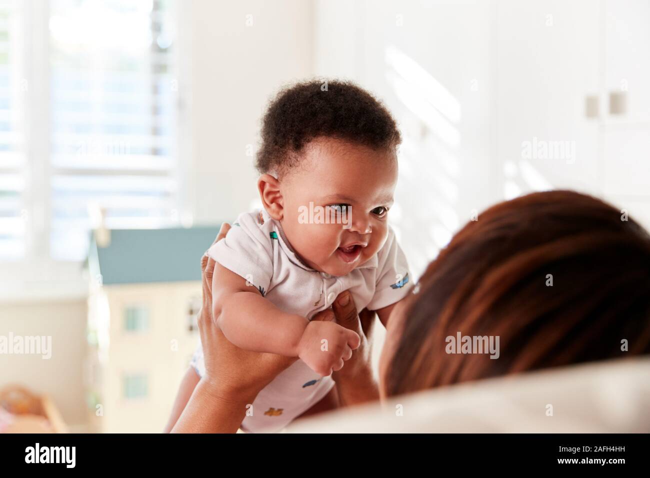 Proud Grandmother Cuddling Baby Grandson In Nursery At Home Stock Photo