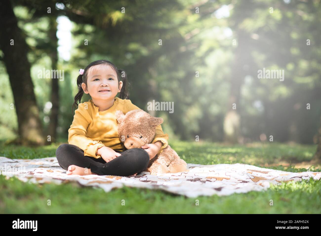 Little asian girl hugging her teddy bear in a park. Concept of happiness and childhood Stock Photo