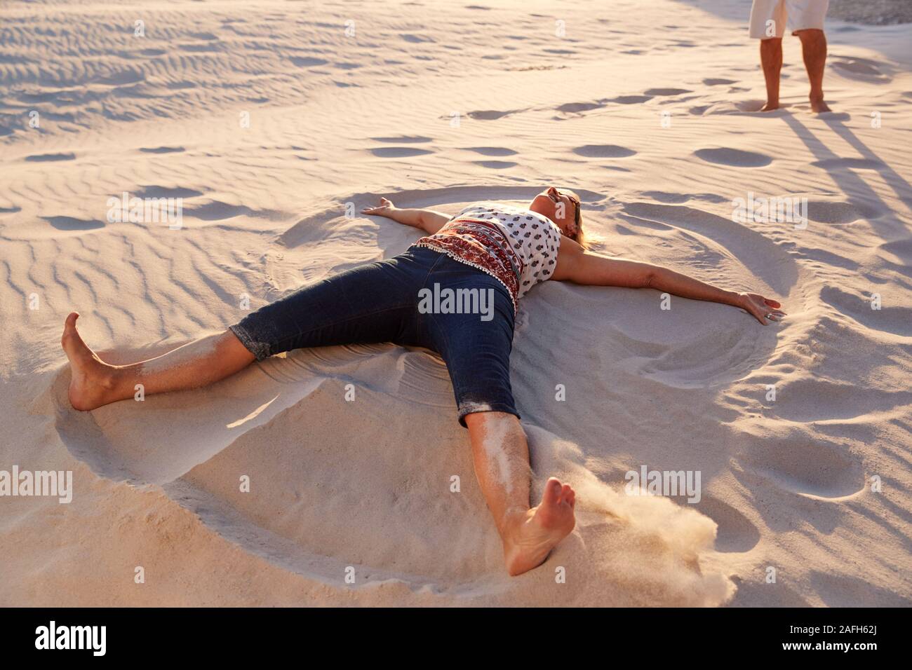 Senior Woman Lying On Beach Making Sand Angel On Vacation Stock Photo