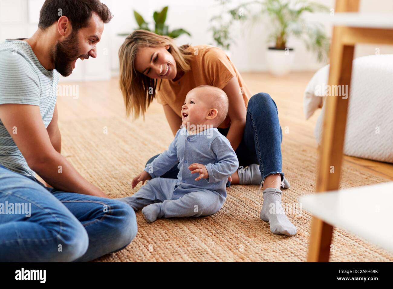 Parents Sitting On Floor At Home Playing With Baby Son Stock Photo