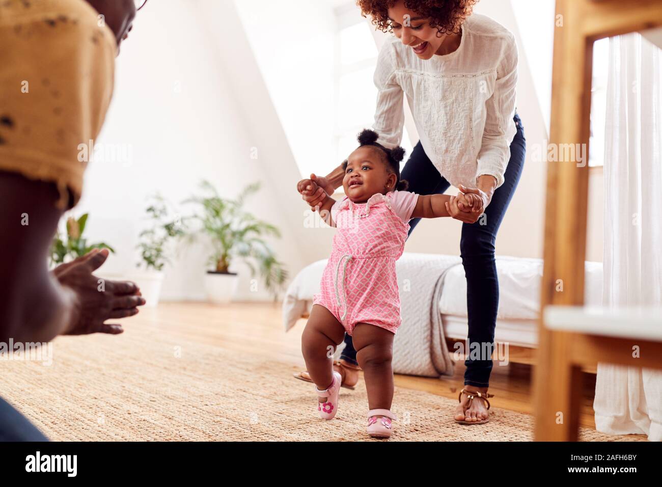 Parents At Home Encouraging Baby Daughter To Take First Steps Stock Photo