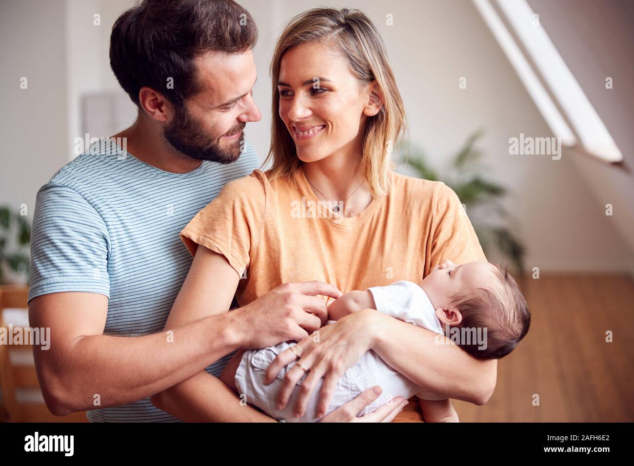 Loving Parents Holding Newborn Baby At Home In Loft Apartment Stock Photo