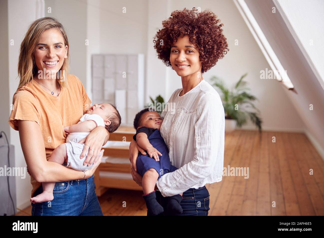 Portrait Of Two Mothers Meeting Holding Newborn Babies At Home In Loft Apartment Stock Photo