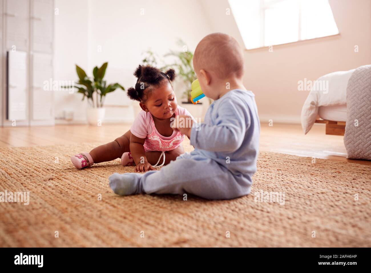 Baby Boy And Girl Playing With Toys On Rug At Home Together Stock Photo