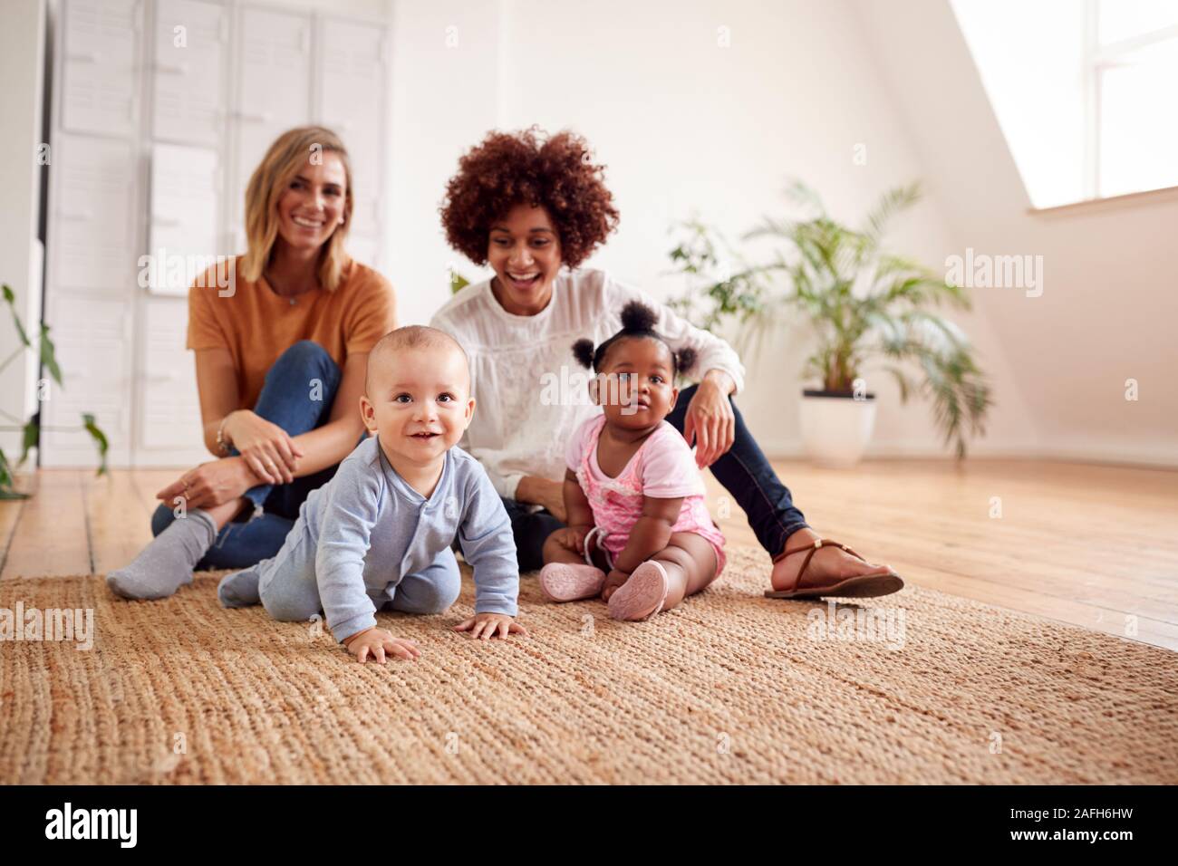 Portrait Of Two Mothers Meeting For Play Date With Babies At Home In Loft Apartment Stock Photo
