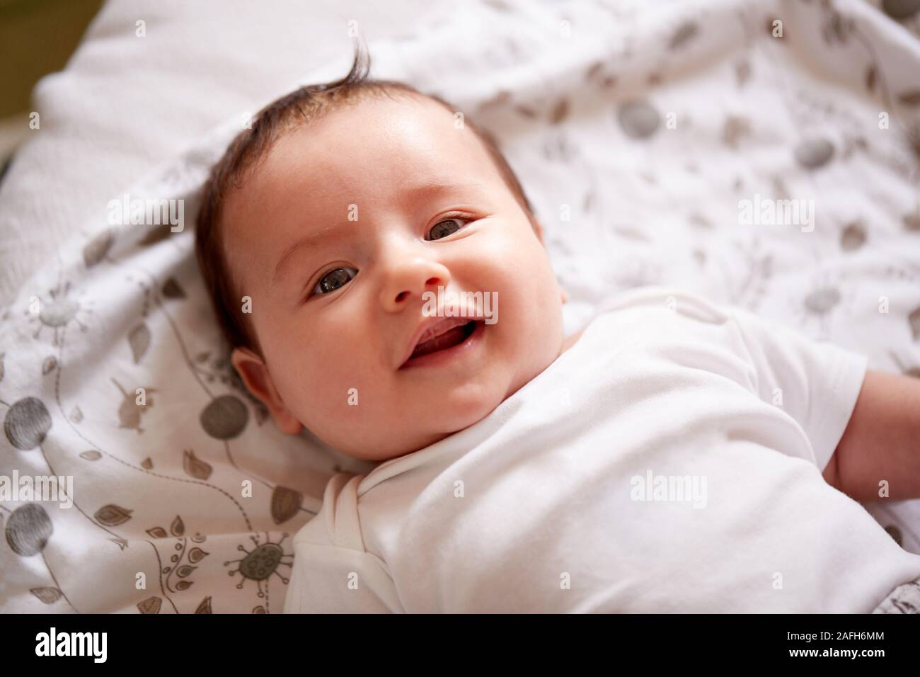 Smiling Baby Boy Lying On Bed At Home Smiling At Camera Stock Photo