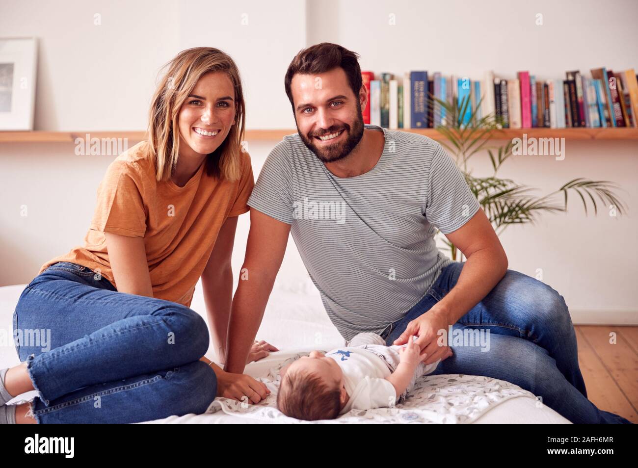 Portrait Of Loving Parents With Newborn Baby Lying On Bed At Home In Loft Apartment Stock Photo
