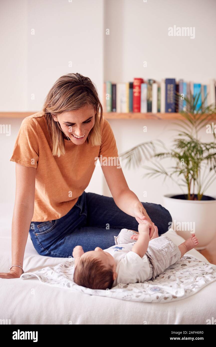 Loving Mother With Newborn Baby Lying On Bed At Home In Loft Apartment Stock Photo