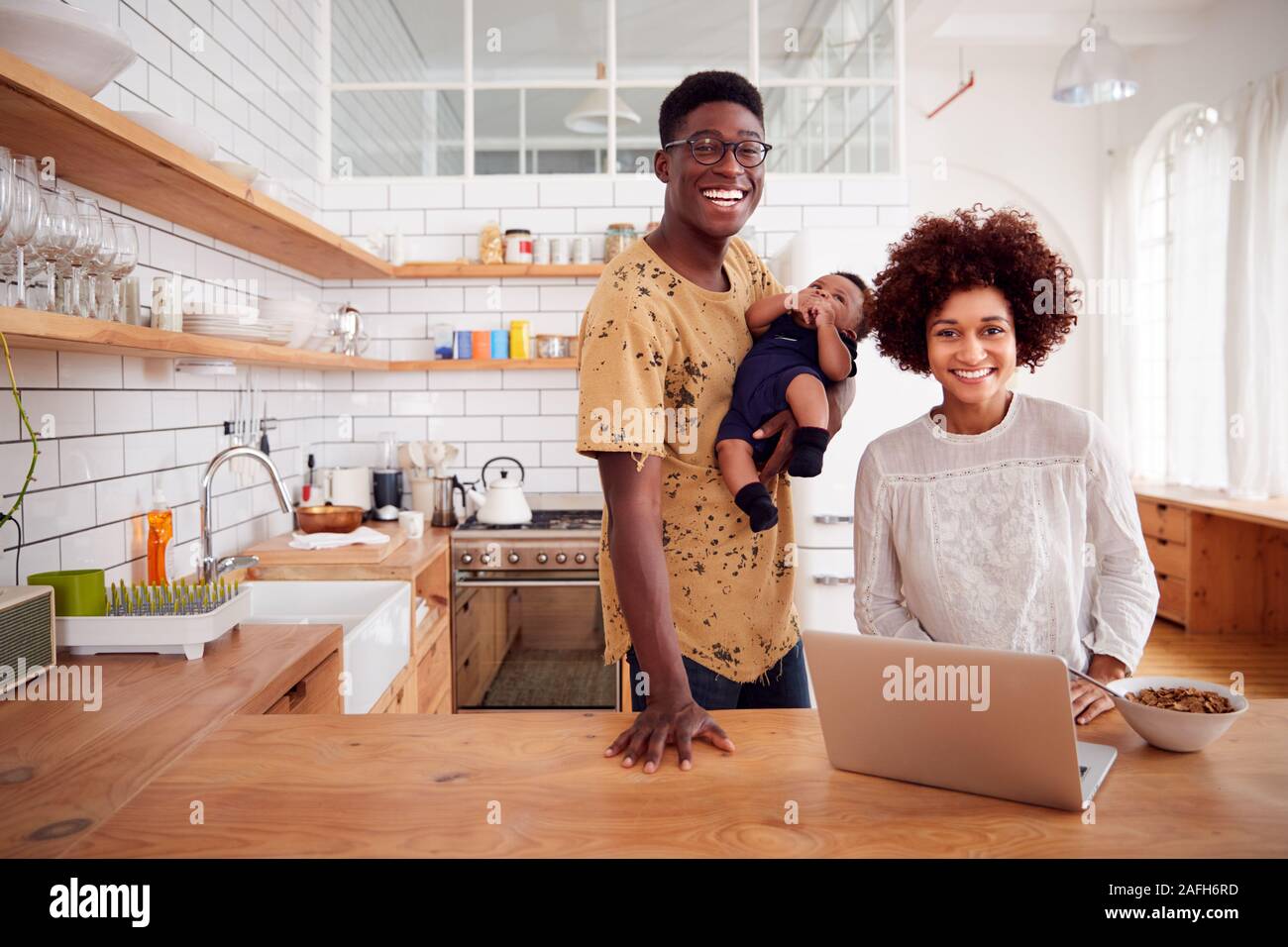 Portrait Of Busy Family In Kitchen At Breakfast With Father Caring For Baby Son Stock Photo