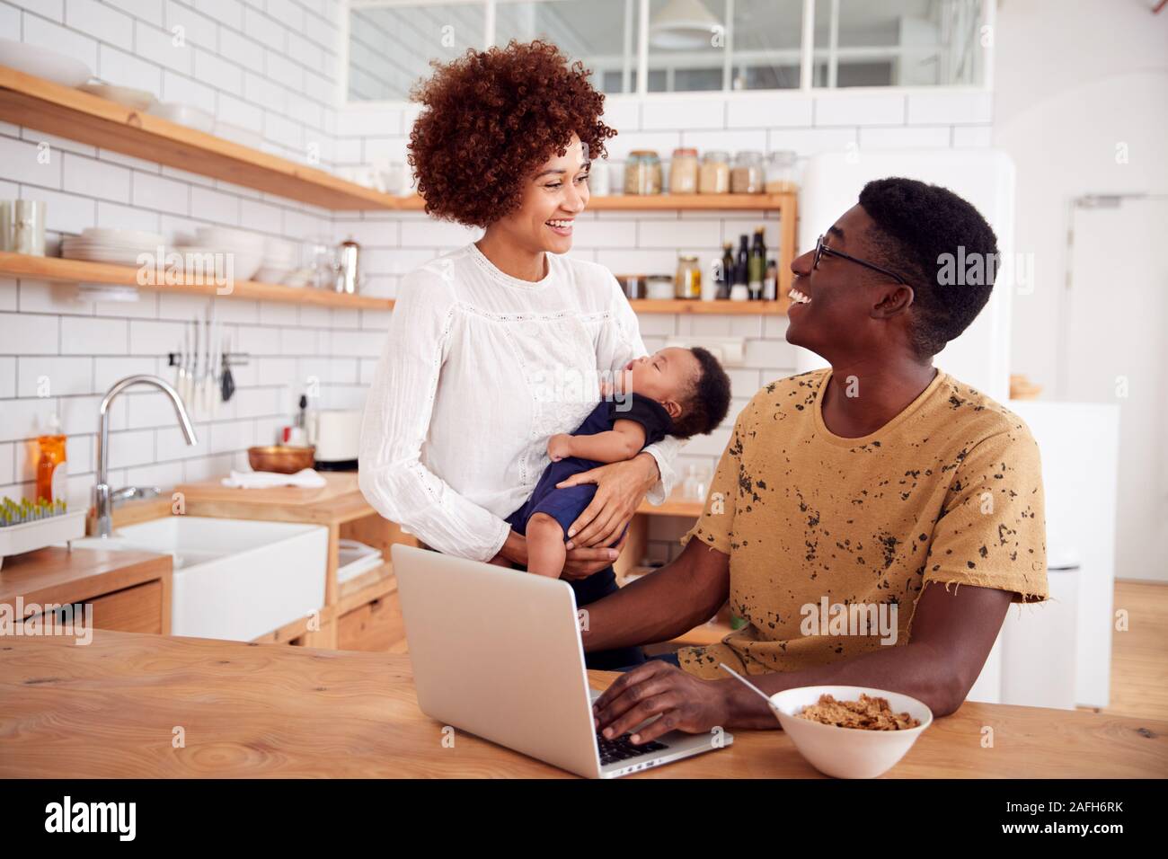Busy Family In Kitchen At Breakfast With Father Caring For Baby Son Stock Photo