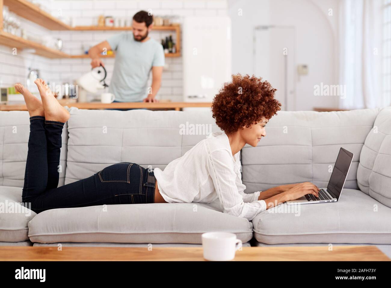 Woman Relaxing Lying On Sofa At Home Looking At Laptop Stock Photo