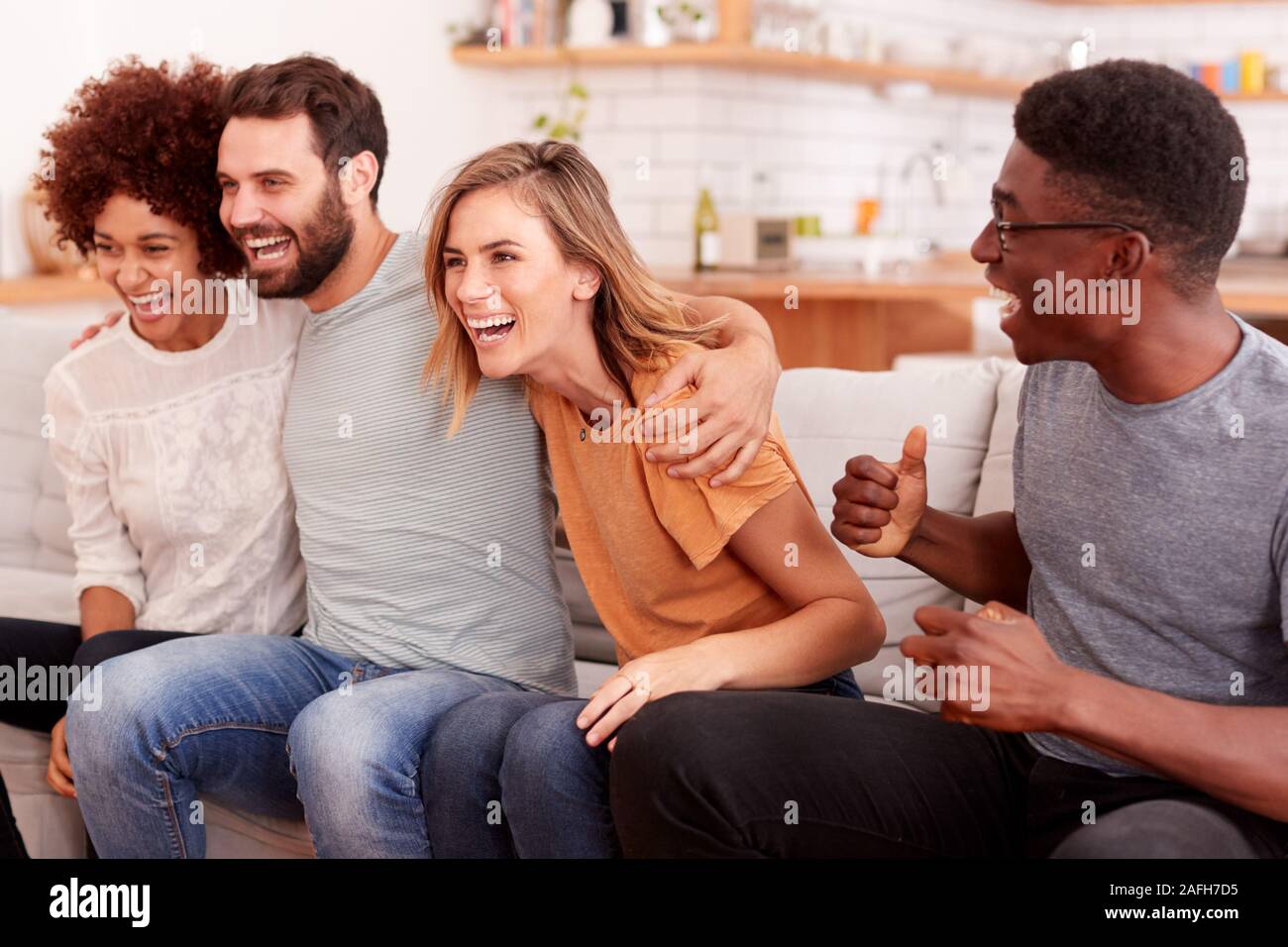 Excited Group Of Friends Sitting On Sofa And Watching Sports On TV Stock Photo