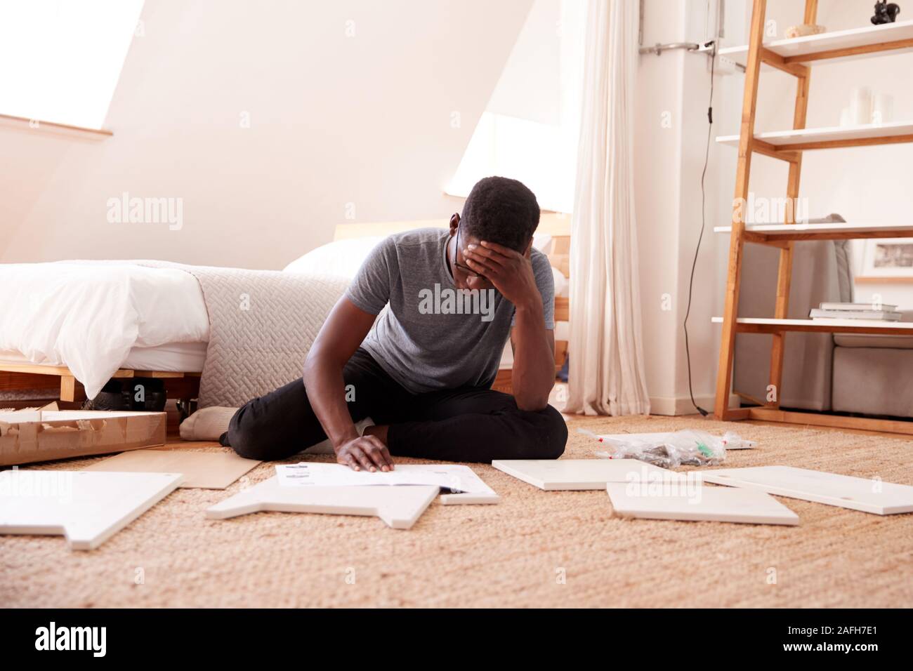 Frustrated Man In New Home Putting Together Self Assembly Furniture Stock Photo