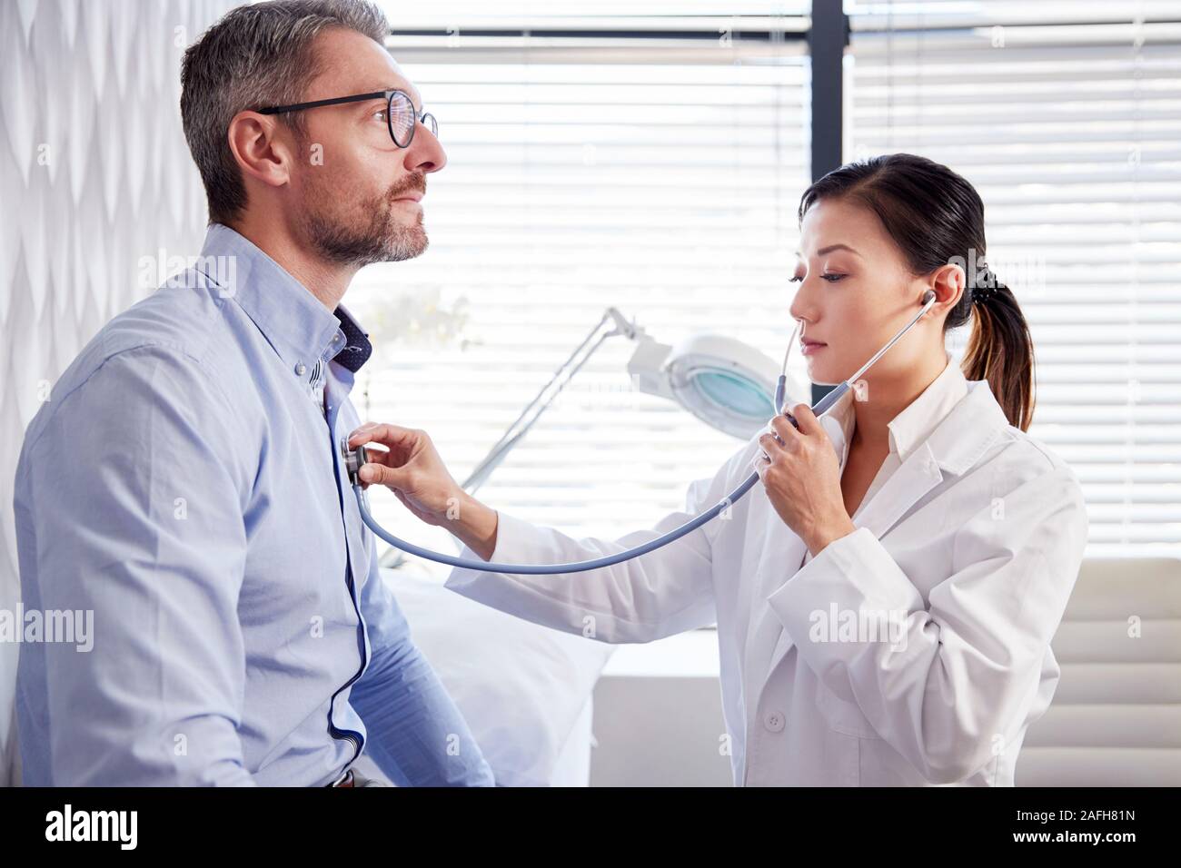 Mature Male Patient Having Medical Exam With Woman Doctor In Office Stock Photo