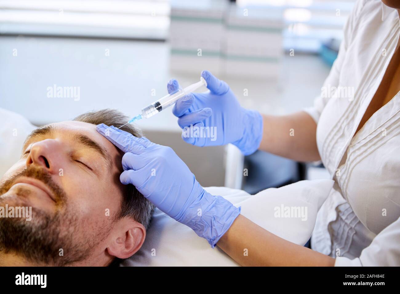 Female Beautician Giving Mature Male Patient Botox Injection In Forehead Stock Photo