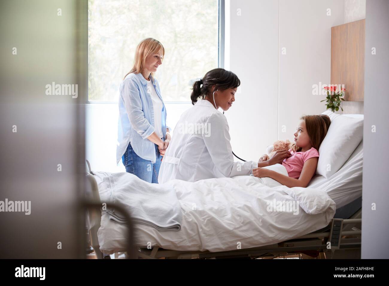 Female Doctor Visiting Mother And Daughter Lying In Bed In Hospital Ward Stock Photo