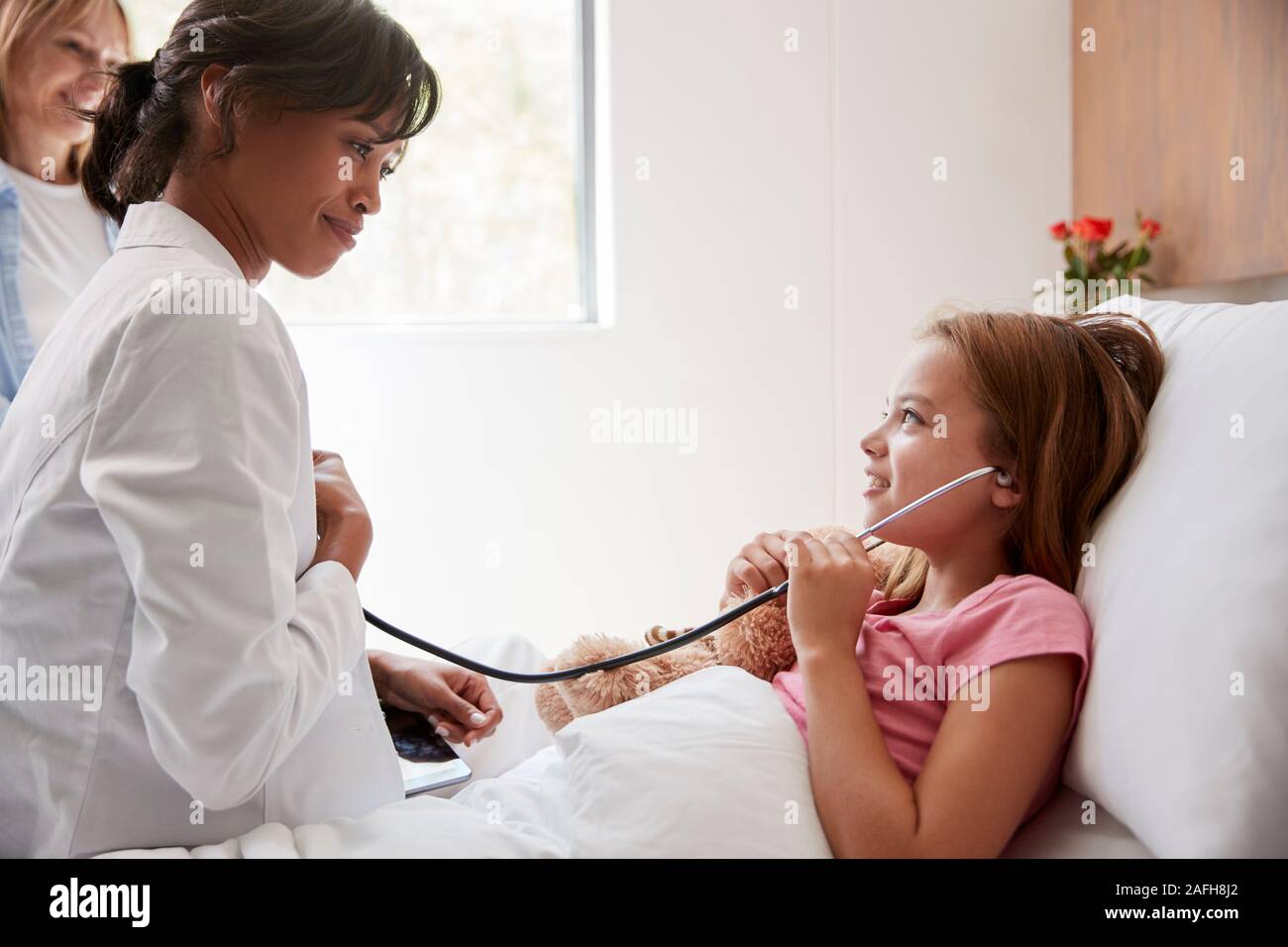 Female Doctor Letting Girl Patient Listen To Her Chest With Stethoscope In Hospital Bed Stock Photo