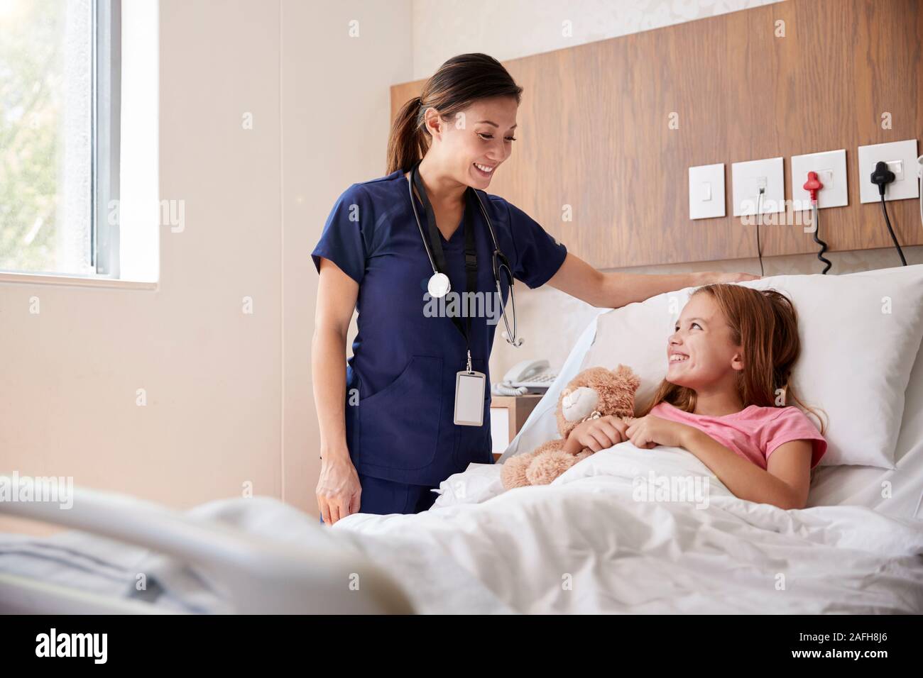Female Nurse Visiting Girl Lying In Hospital Bed Hugging Teddy Bear Stock Photo