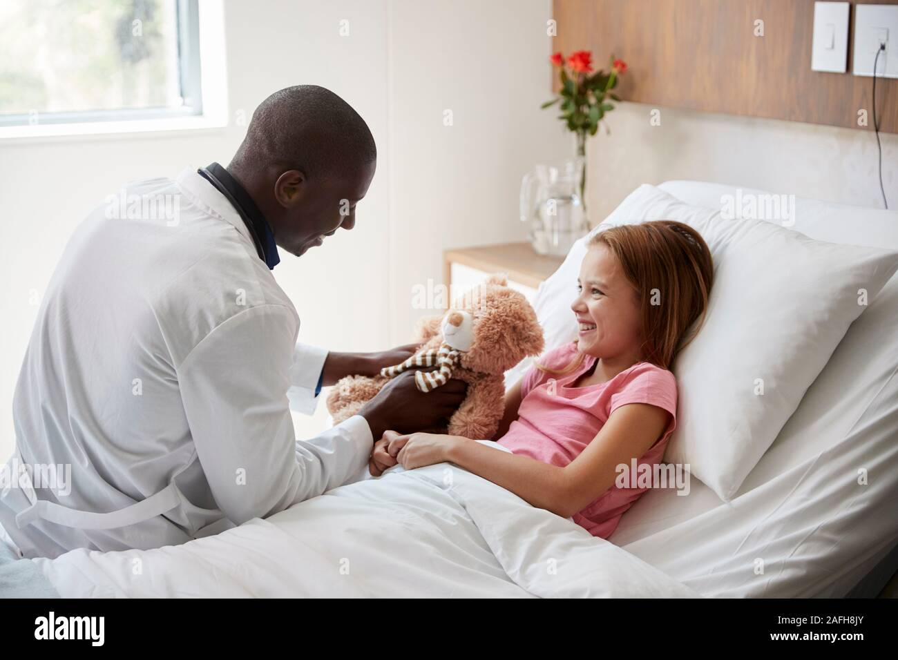 Male Doctor Visiting Girl Lying In Hospital Bed Hugging Teddy Bear