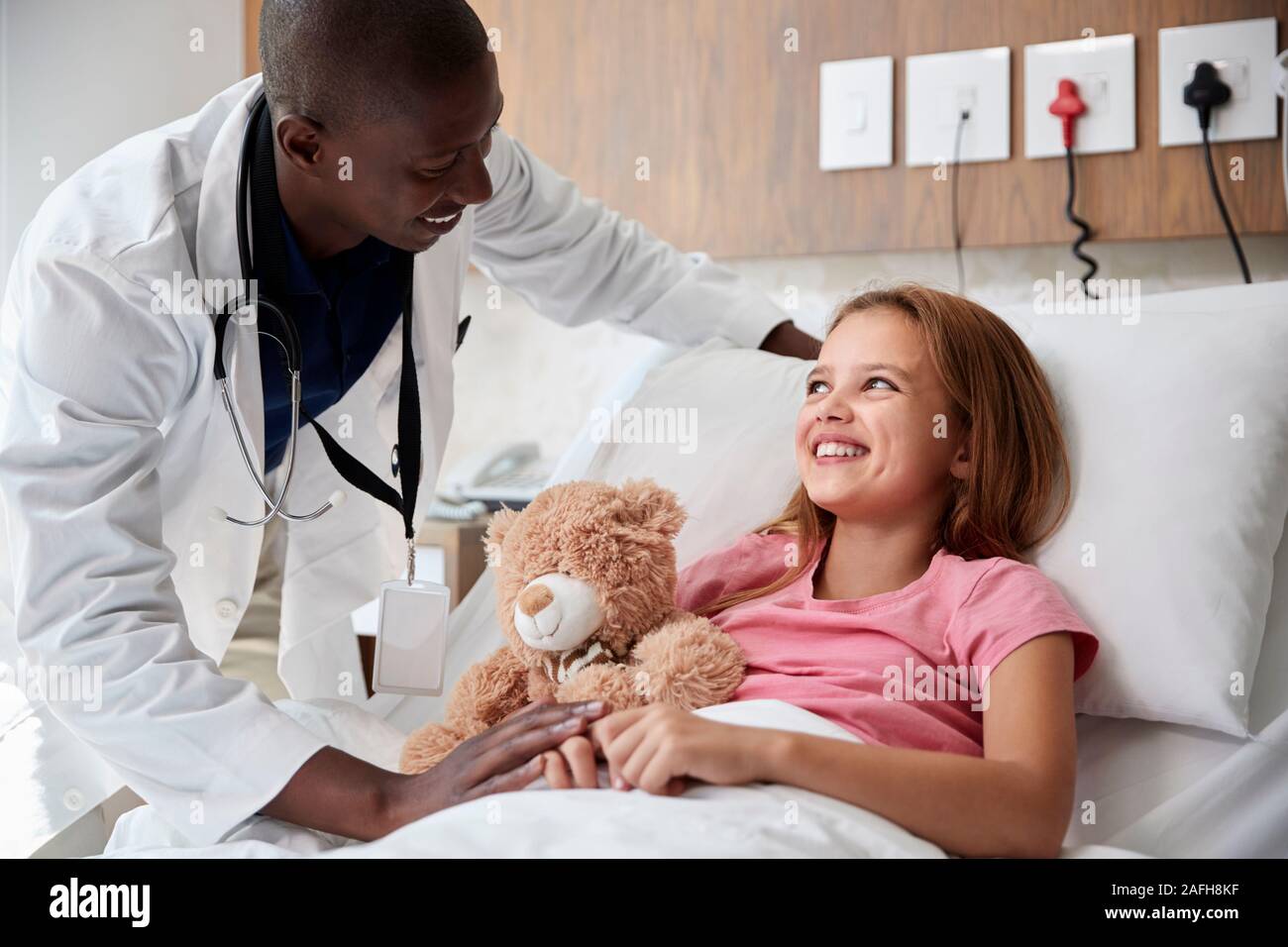 Male Doctor Visiting Girl Lying In Hospital Bed Hugging Teddy Bear Stock Photo