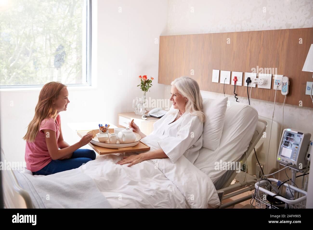 Granddaughter Visiting Grandmother In Hospital Bed For Afternoon Tea Stock Photo