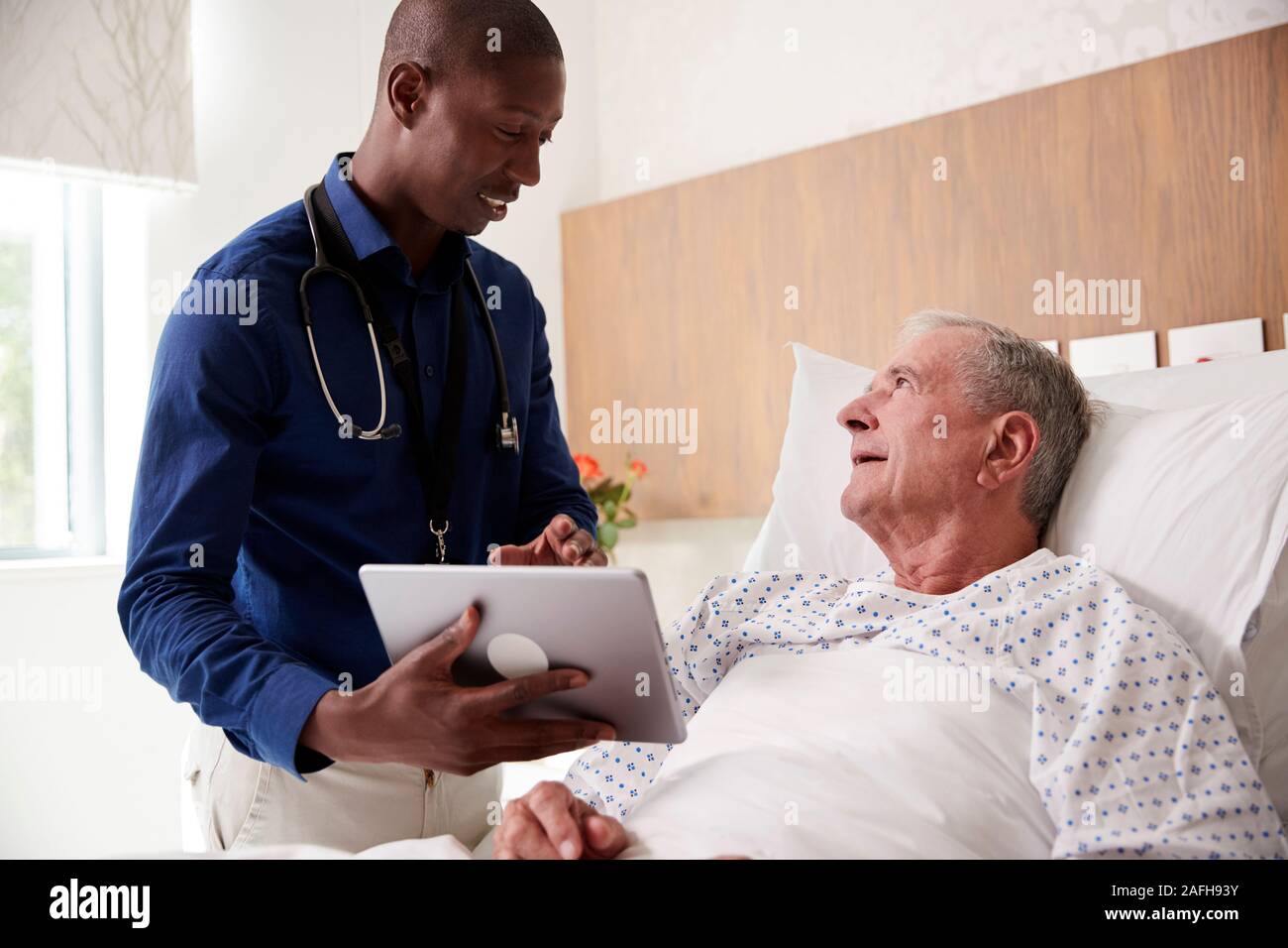 Doctor With Digital Tablet Visiting And Talking With Senior Male Patient In Hospital Bed Stock Photo