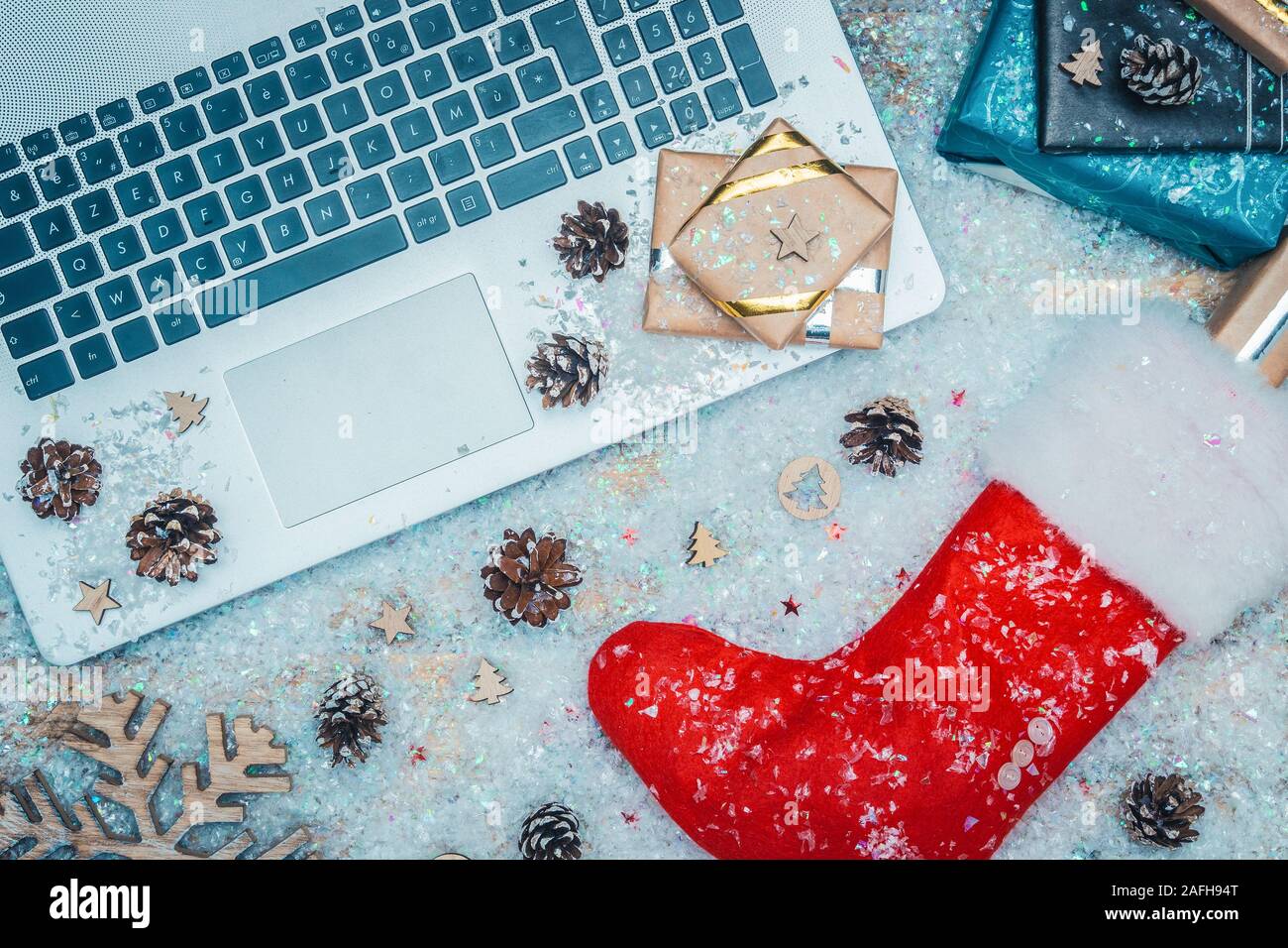 Flat lay or top view of laptop keyboard, gifts and red Santa Claus sock on fake snow. Online shopping for christmas holiday concepts. Stock Photo