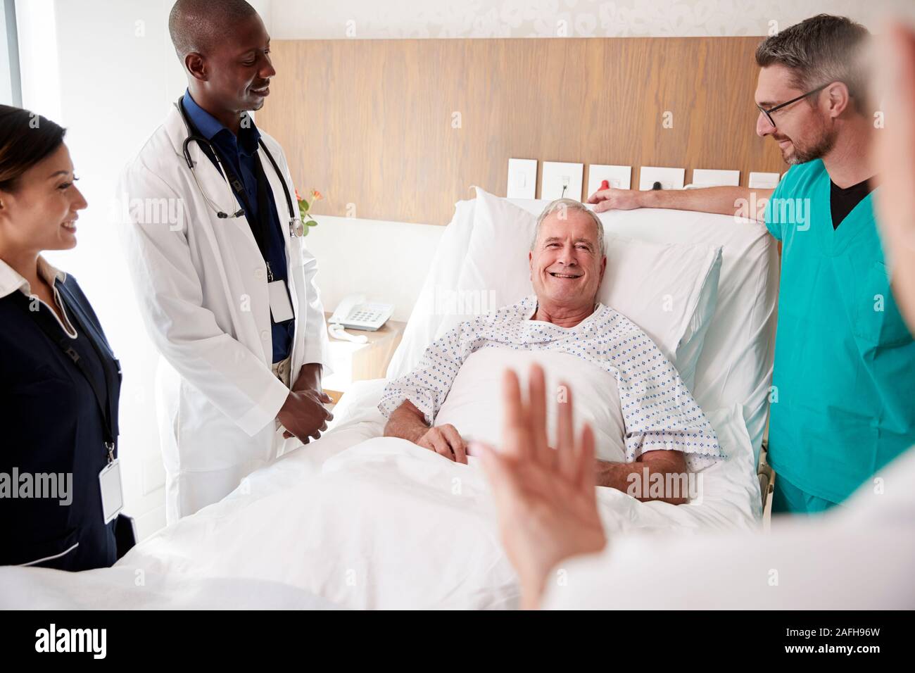 Medical Team On Rounds Meeting Around Bed Of Senior Male Patient Stock Photo