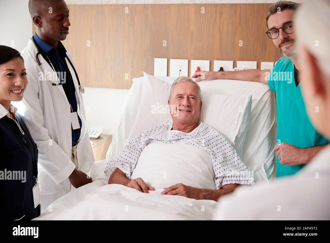 Medical Team On Rounds Meeting Around Bed Of Senior Male Patient Stock Photo