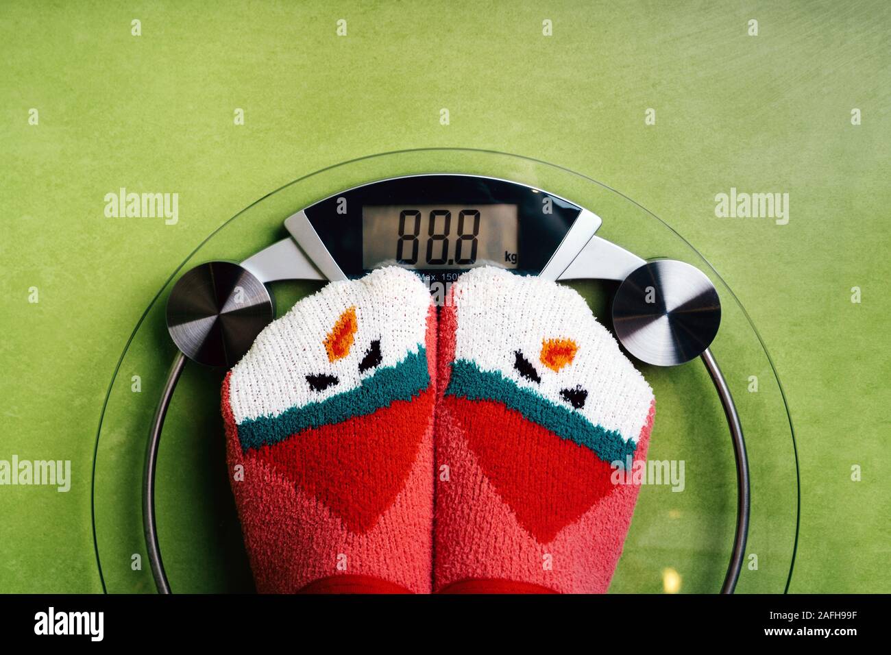 Girl standing on the scales in Christmas fun red green socks with snowman Stock Photo