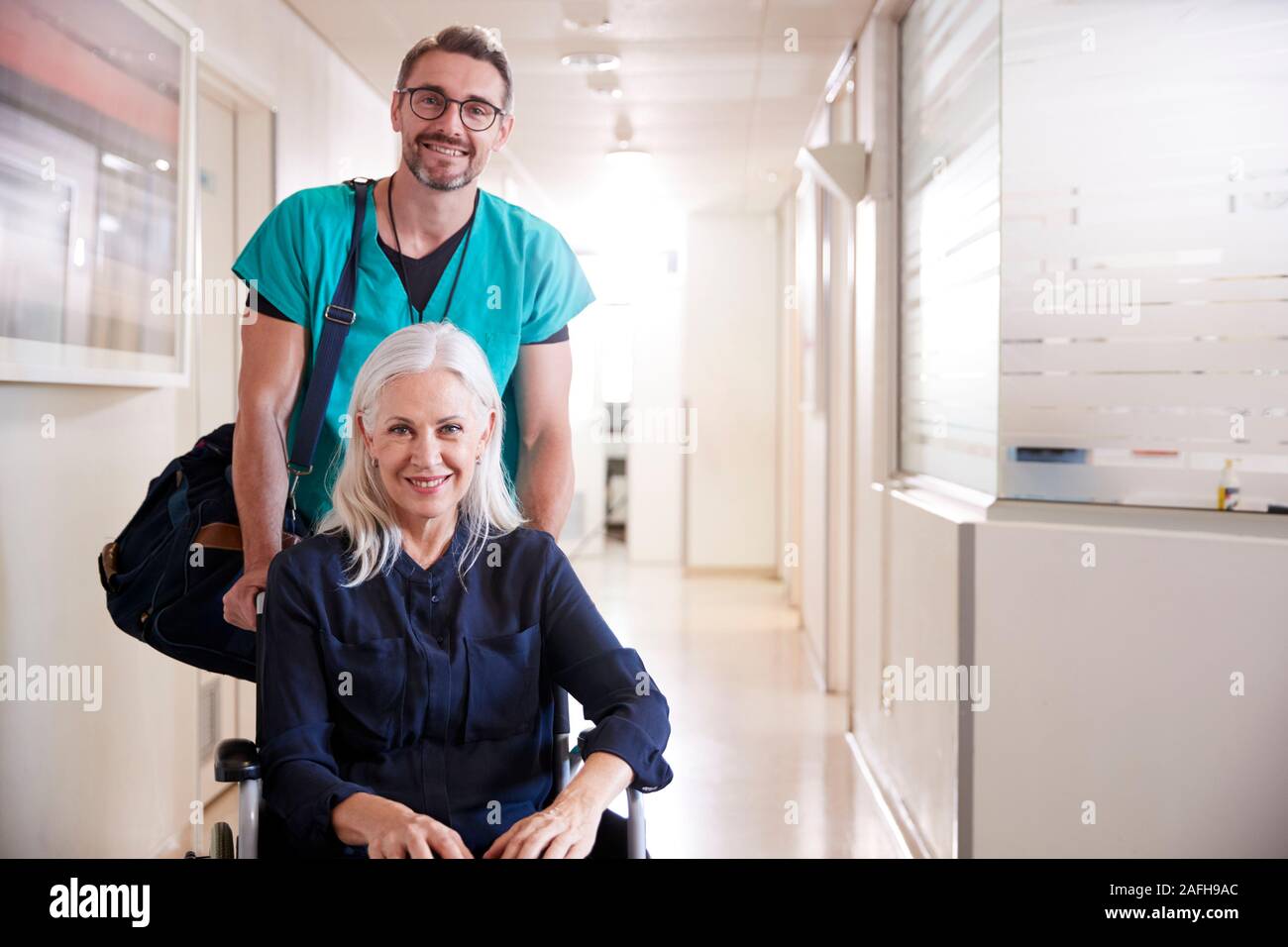 Male Orderly Pushing Senior Female Patient Being Discharged From Hospital In Wheelchair Stock Photo