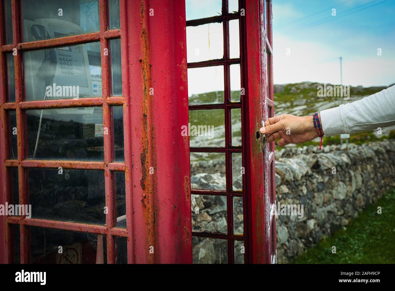 Mans hand opening door to remote traditional red telephone box on the Isle of Harris, Outer Hebrides, Scotland Stock Photo