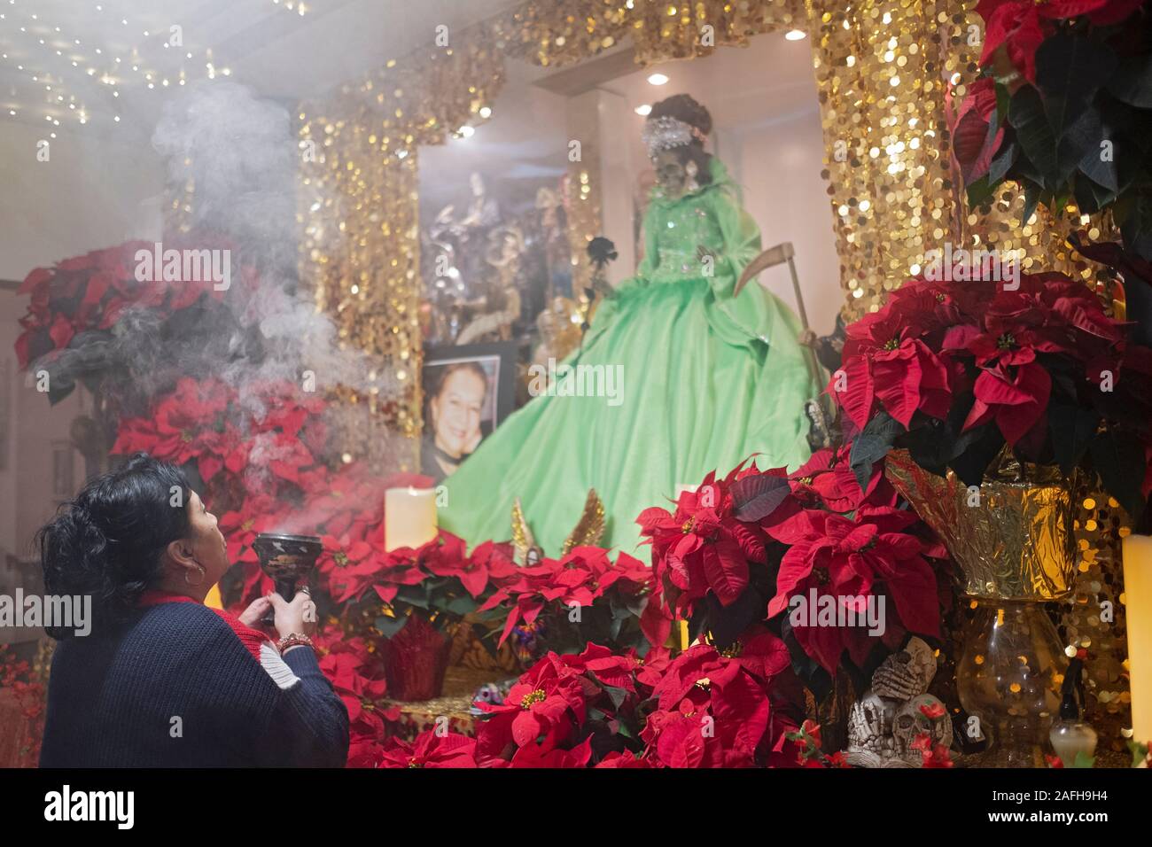 A Santa Muerte devotee prays at a home temple in Jackson Heights, Queens, New York City. She blows smoke at a deity as is a custom. Stock Photo