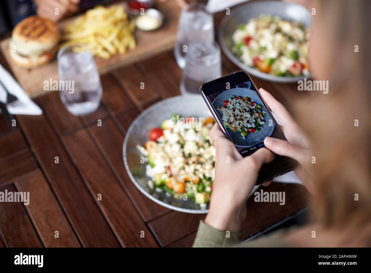 Female Friends In Restaurant Taking Picture Of Food In Restaurant To Post On Social Media Stock Photo