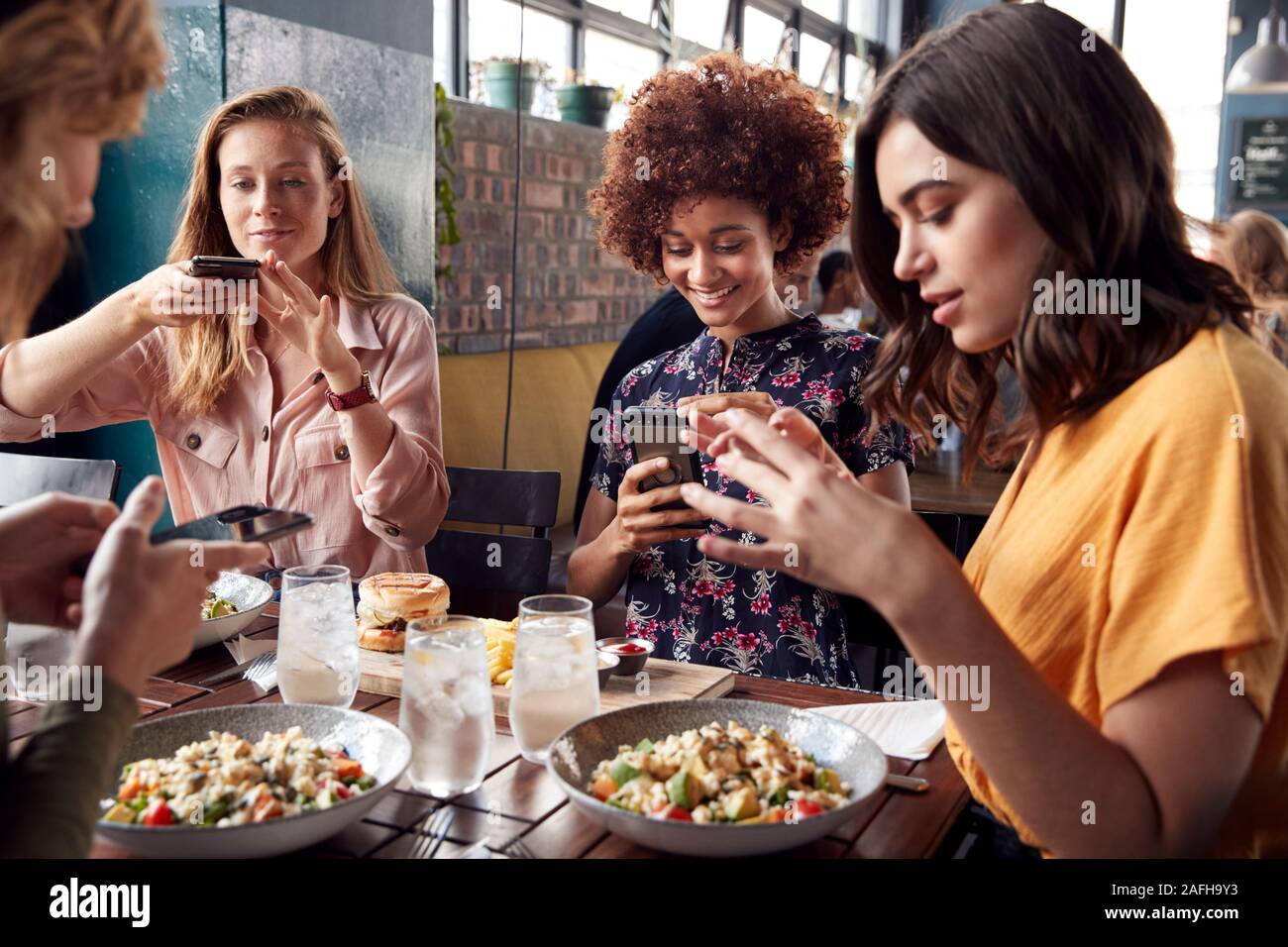 Female Friends In Restaurant Taking Picture Of Food In Restaurant To Post On Social Media Stock Photo