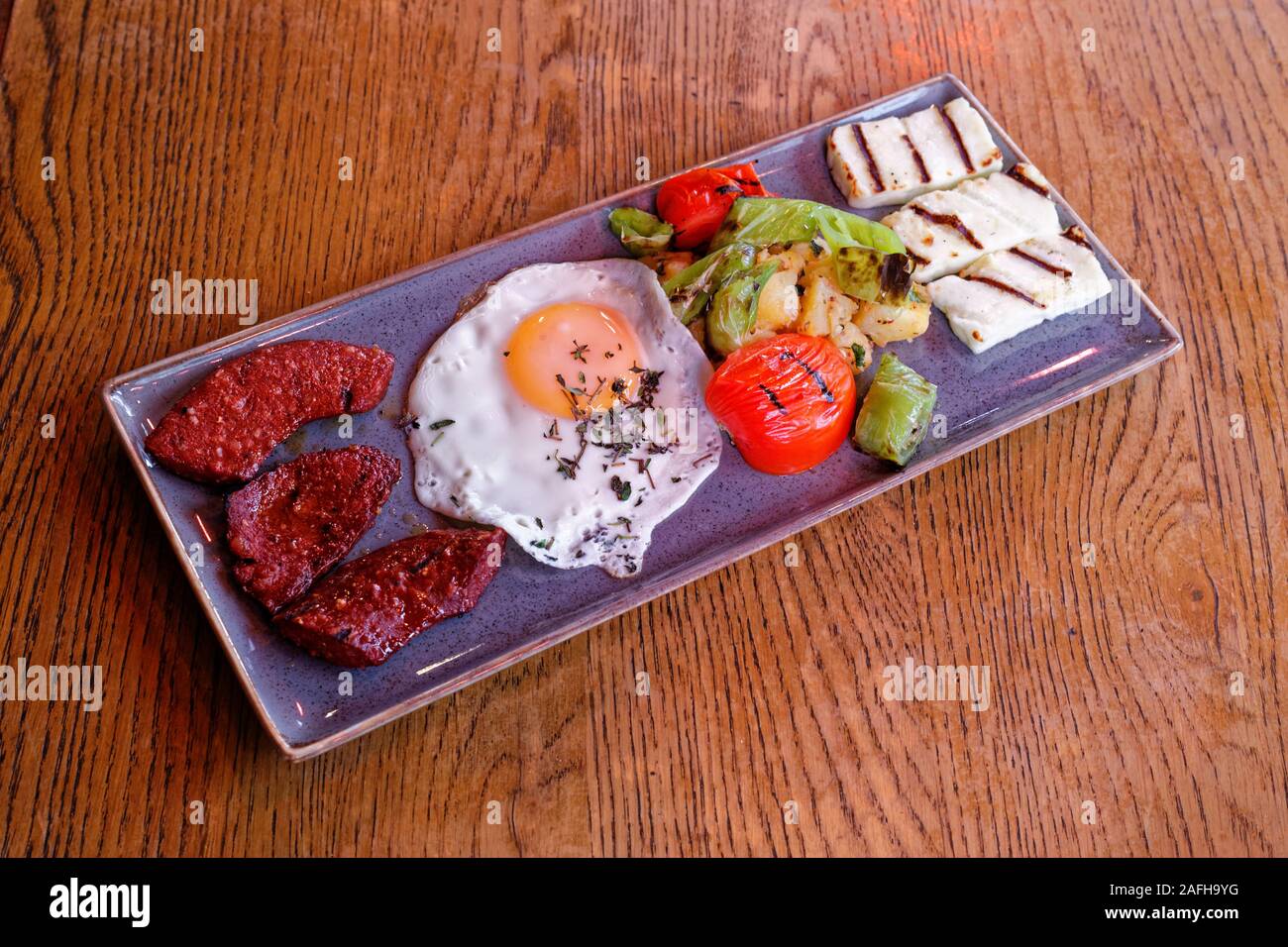 Turkish roasted breakfast plate with fermented bologna sausage (sudjuk), grilled egg, hallouim (hellim) cheese, boiled potatoe, green pepper, tomato. Stock Photo