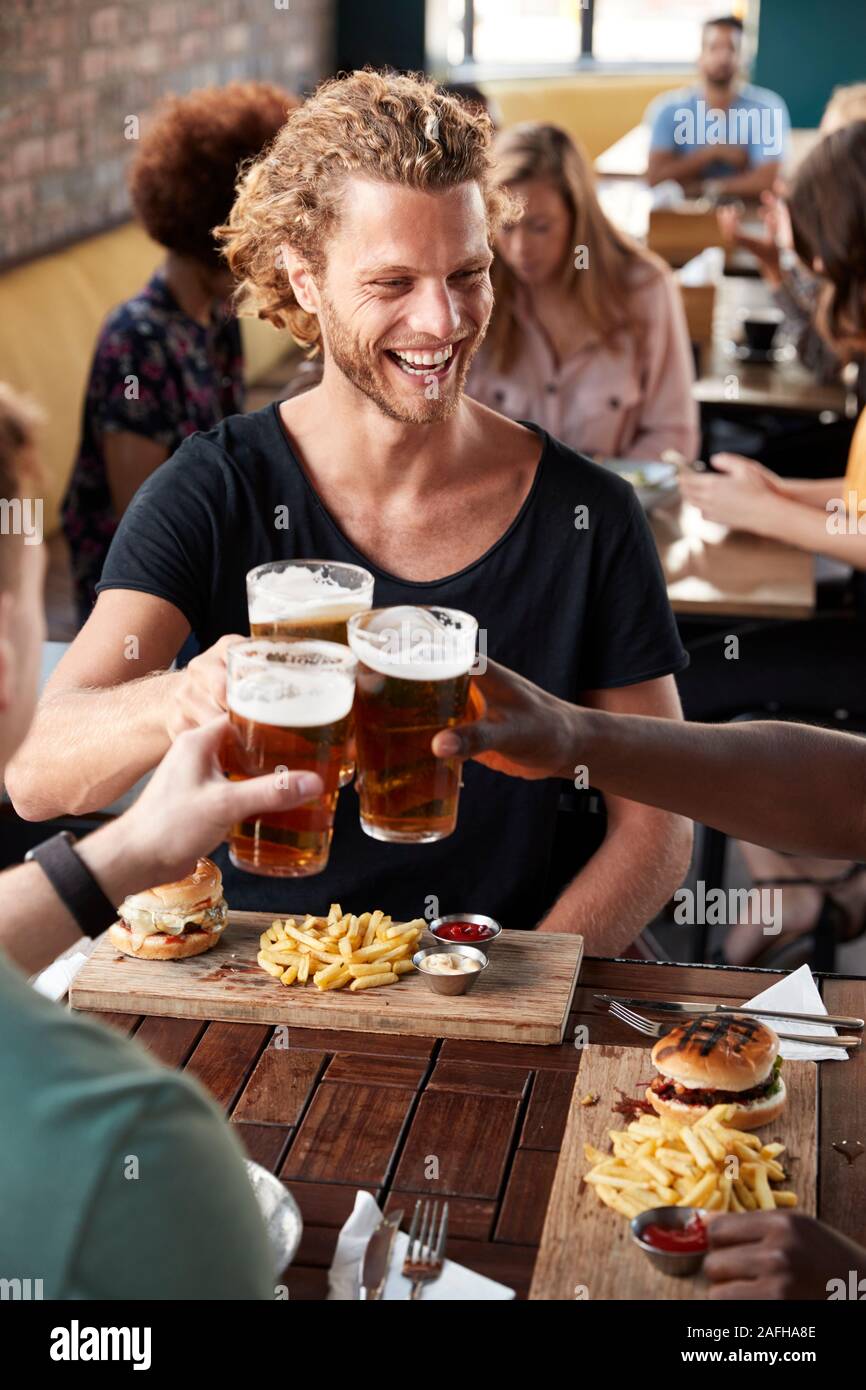 Three Young Male Friends Meeting For Drinks And Food Making A Toast In Restaurant Stock Photo