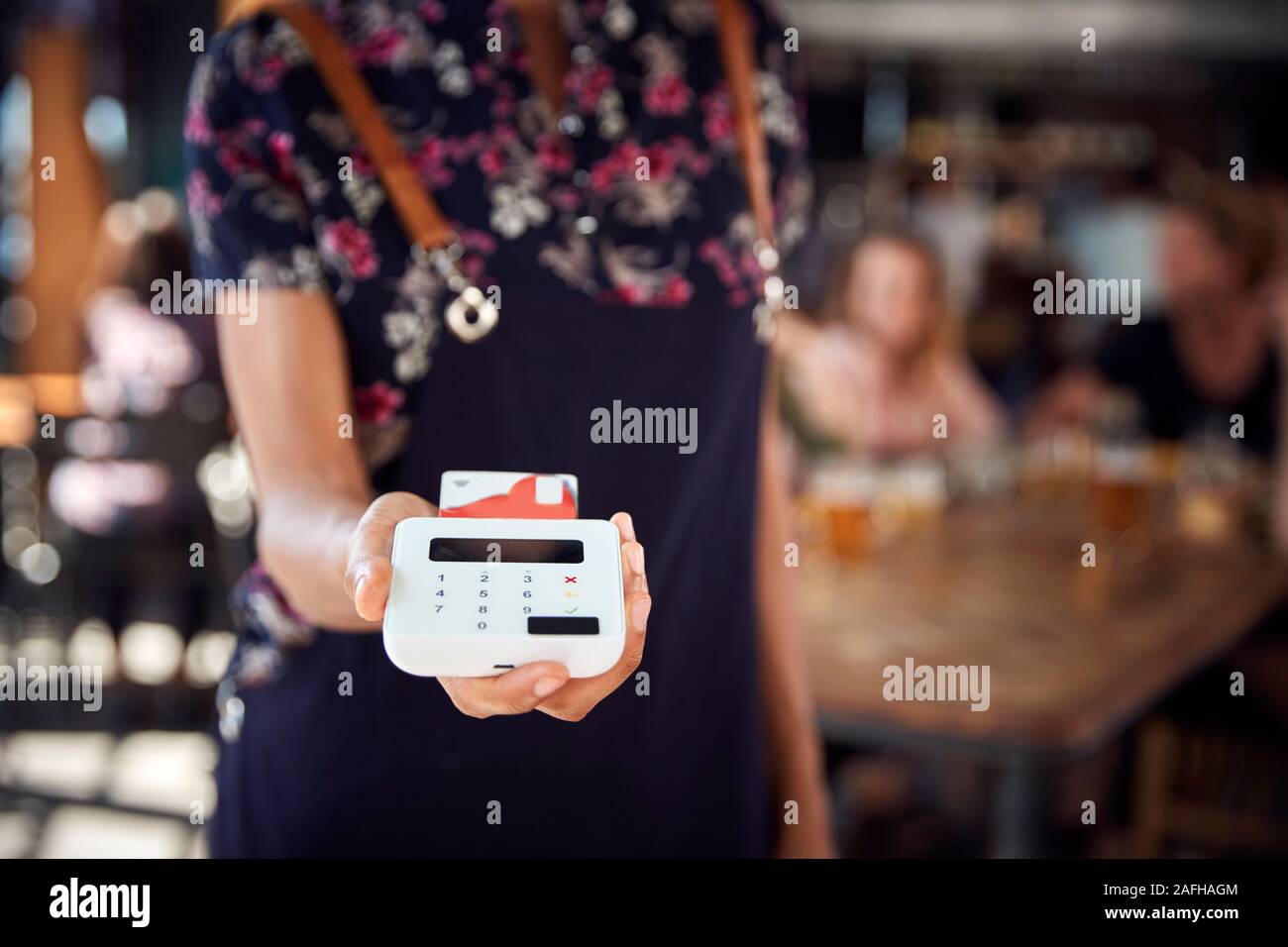 Close Up Of Waitress Holding Credit Card Payment Terminal In Busy Bar Restaurant Stock Photo