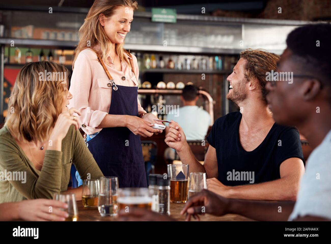 Waitress Holds Credit Card Machine As Customer Pays Bill In Bar Restaurant Stock Photo
