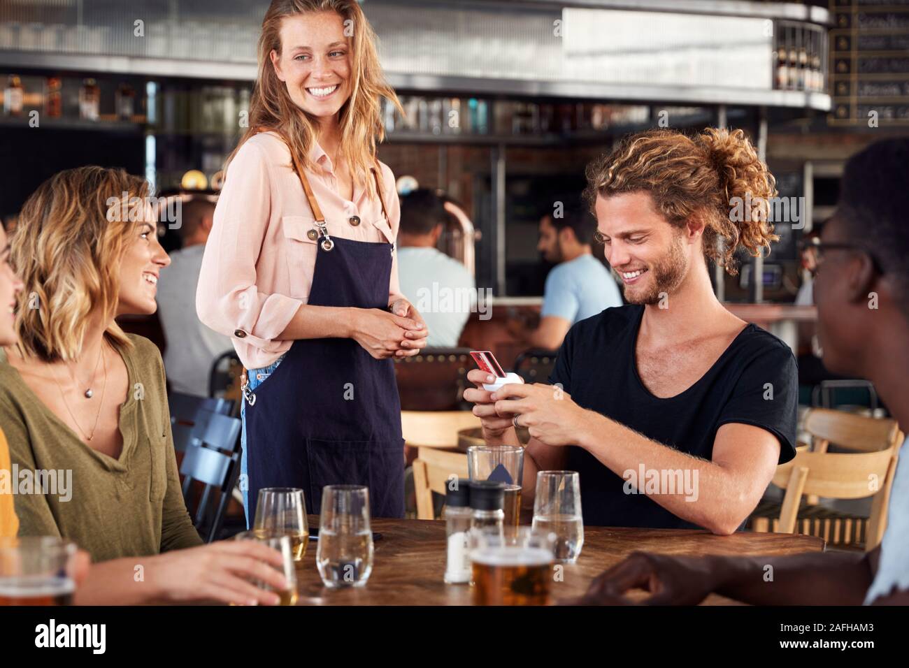 Waitress Holds Credit Card Machine As Customer Pays Bill In Bar Restaurant Stock Photo