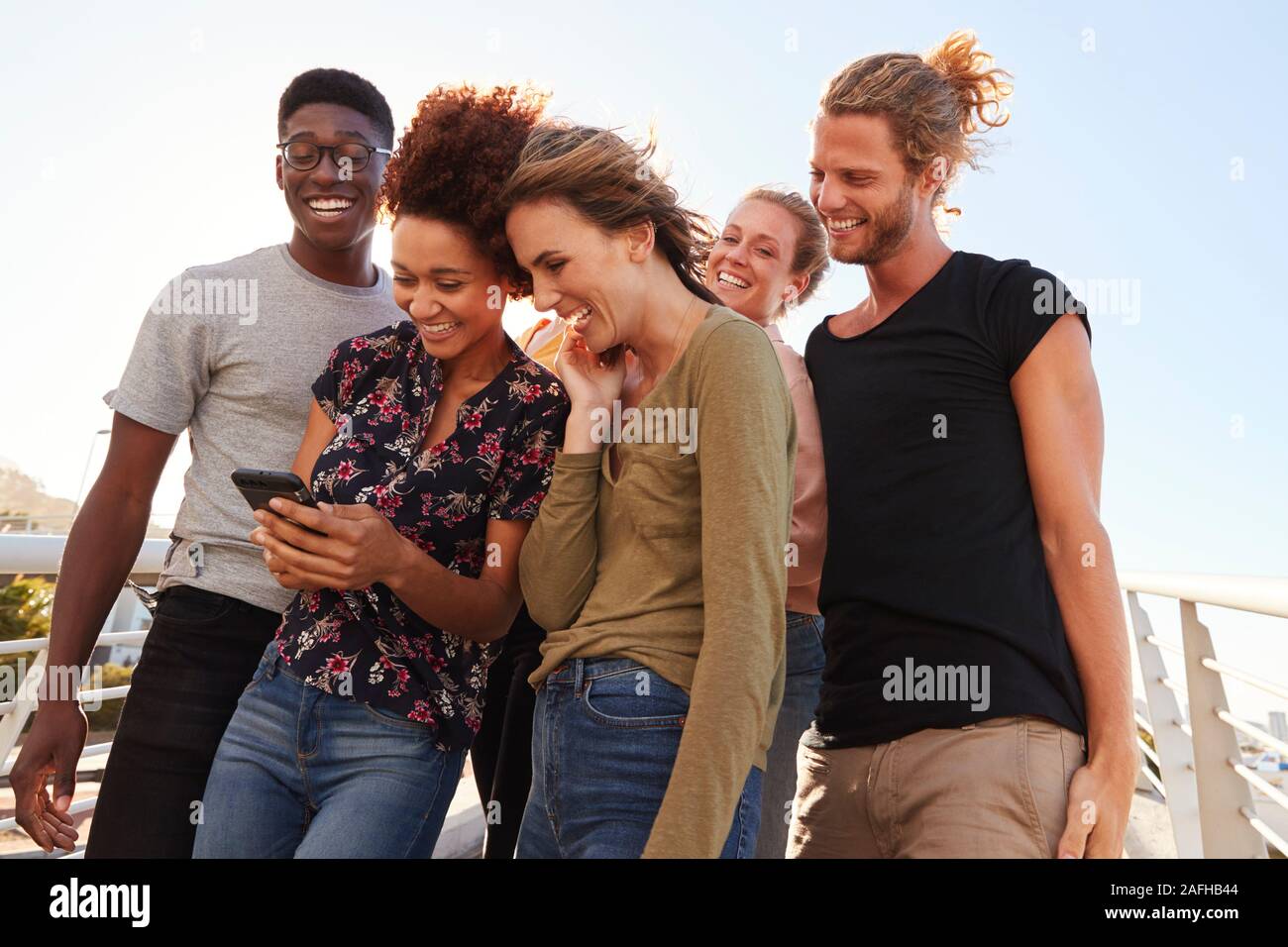 Smiling Young Friends Looking At Selfie On Outdoor Footbridge Together Stock Photo